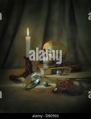 Skull, magnifying glass, candle and books on table Stock Photo