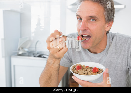 Happy man eating cereal for breakfast in kitchen Stock Photo