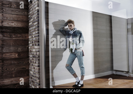 Young woman leaning against wall looking out of window Stock Photo