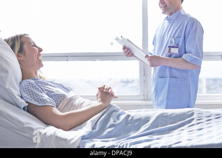 Patient lying in hospital bed laughing with nurse Stock Photo