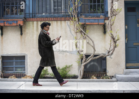 A woman in a warm coat walking along the street checking her phone Stock Photo