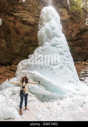 Woman stands by giant ice cone that has formed at the base of the waterfall at Ash Cave, Hocking Hills State Park Stock Photo