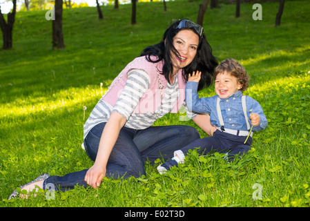 Mother and her son having fun in grass and the toddler waving hand Stock Photo