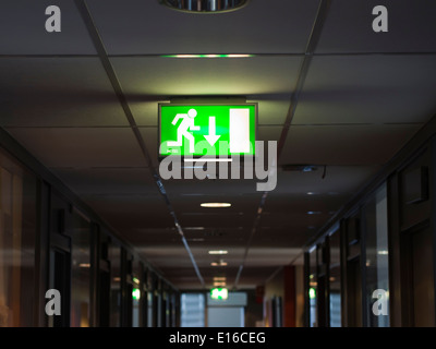 Green lit emergency exit sign in ceiling of dark corridor, this way out Stock Photo