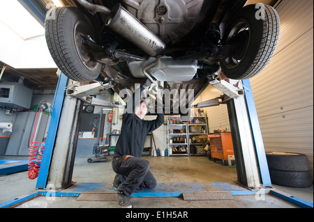 A mechanic is checking the exhaust of a car who is lifted up in a repair service station. Stock Photo