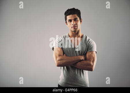 Portrait of young muscular man posing against grey background. Handsome young hispanic male model standing with his arms crossed Stock Photo