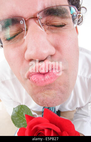 Guy wearing glasses trying to be romantic giving a kiss holding rose with his eyes closed Stock Photo