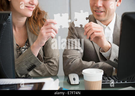 Business people putting puzzle pieces together at desk Stock Photo