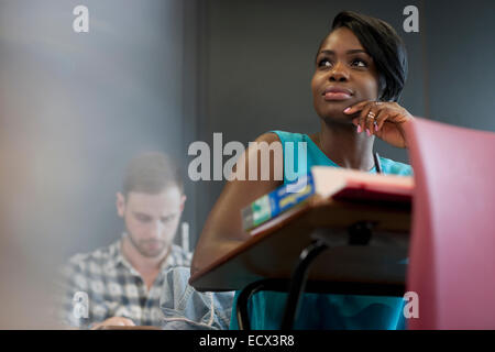 University student sitting at desk with hand on chin Stock Photo