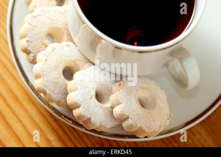 Italian butter biscuits on a saucer of a cup of black tea. These cookies have a daisy shape and are sprinkled with powdered suga Stock Photo