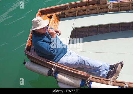 Ferry man on mobile phone relaxing on rowing boat in the sun waiting for passengers  at Weymouth, Dorset in June Stock Photo