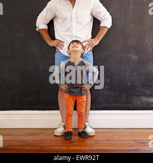 Indoor shot of little boy looking at his father while standing in front with hands on waist. Stock Photo