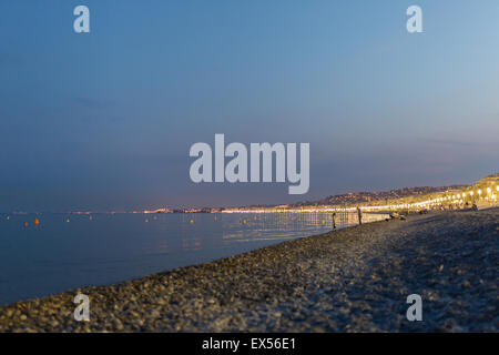 Illuminated beach promenade at night in Nice with blurred people playing in the background Stock Photo