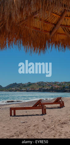 Straw thatch tiki hut and lounge chairs on a sandy beach Stock Photo