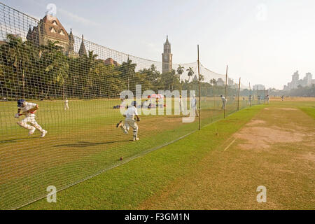 Children playing cricket in the Oval maidan with Rajabai Tower and High Court in the background ; Bombay Mumbai Maharashtra Stock Photo