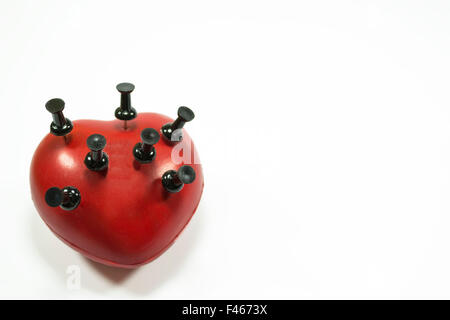 Red heart shape with black push pins puncturing it , conceptual image about heart related medical illnesses Stock Photo