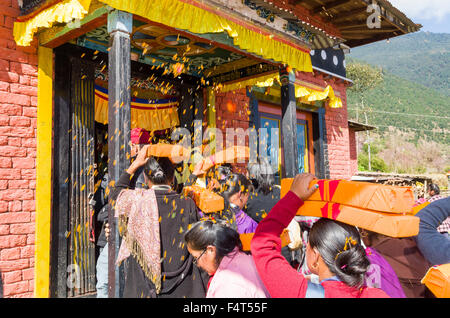 People carrying tibetan prayer books, wrapped in yellow material, on their heads at Lhapab Tuchen festival. Stock Photo