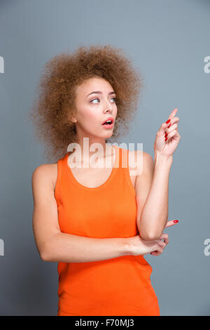 Amazed shocked pretty young curly woman in orange top pointing away on copyspace Stock Photo