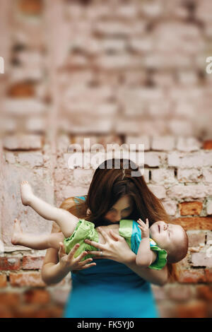 Portrait of Loving Young Mother Holding and Kissing Her Baby against Brick Wall. Selective Focus, Tilt Shift Blurred Effect. Stock Photo