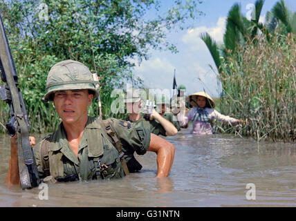 U.S Army soldier PFC Fred Greenleaf, with C Company, 3rd Battalion, 7th Infantry division, 199th Light Infantry Brigade, crosses a deep irrigation canal along with members of the 5th ARVN Ranger Group enroute to a Viet Cong controlled village during operation Rang Dong November 21, 1967 in Cat Lai , South Vietnam. Stock Photo