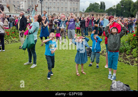 Tourists looking up to the sky watching a fly past on the gardens outside Buckingham Palace. Stock Photo