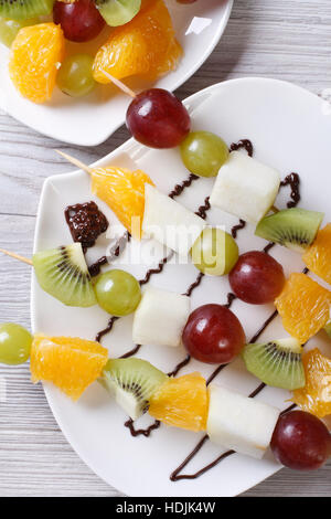 Fresh fruit on skewers with chocolate sauce closeup. vertical top view Stock Photo