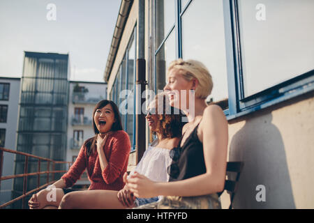 Shot of smiling young female friends sitting together in terrace. Multiracial women relaxing outdoors and having fun. Stock Photo