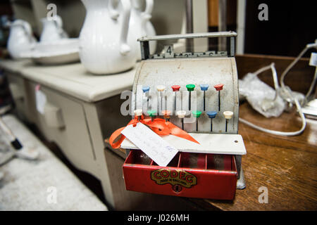 Lovely well-loved old metal vintage children's toy cash register for sale in an antique shop with colourful tabs and a red cash drawer. Stock Photo