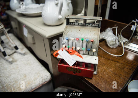 Lovely well-loved old metal vintage children's toy cash register for sale in an antique shop with colourful tabs and a red cash drawer. Stock Photo