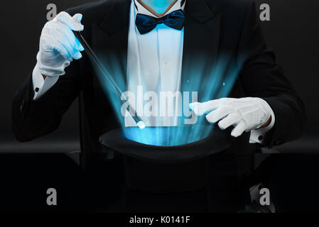 Midsection of magician holding magic wand over illuminated hat against black background Stock Photo