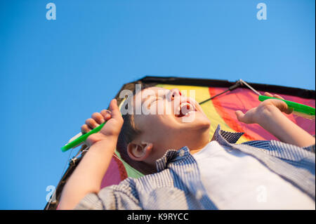 Laughing cheerful boy holding a kite over his head against a blue sky Stock Photo