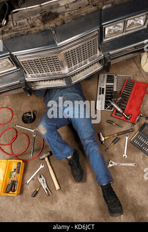 Photo of a mechanic doing repairs under the front of an old car from the early 80's. Stock Photo