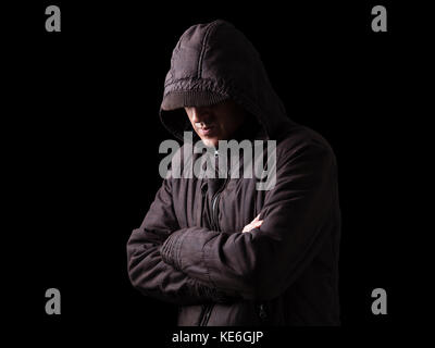 Lonely, depressed, fragile man hiding face, arms crossed, standing in the darkness. Low key, black background / Loneliness unhappy upset depression Stock Photo