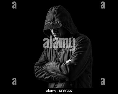 Lonely, depressed, fragile man hiding face, arms crossed, standing in the darkness. Low key, black background / Loneliness unhappy upset depression Stock Photo