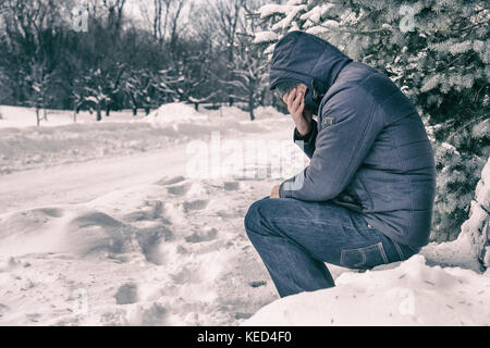 Man sitting on bench in a forest in winter with snow on the ground Stock Photo