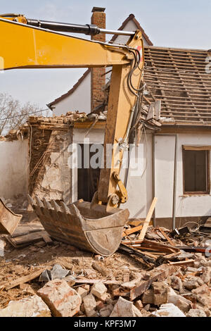 A large track hoe excavator tearing down an old house Stock Photo