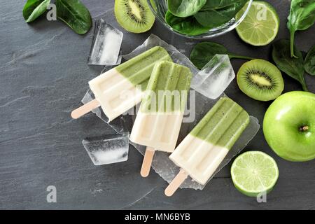 Group of green smoothie popsicles with kiwi, spinach, apple and limes, above view on a dark slate background Stock Photo