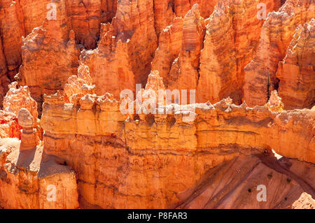 One person on footpath through pinnacles, rock faces and hoodoos shows the scale of this unusual orange-red landscape in Bryce Canyon National Park Stock Photo