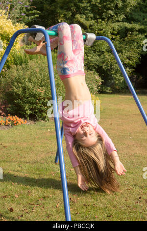 six year old girl doing gymnastics acrobatics on apparatus in back garden for play, UK. Stock Photo