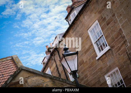 Looking up towards the tops of old street lamps with walls, street signs and blue sky backgrounds in Scarborough and Robin Hood's Bay, Yorkshire, UK Stock Photo