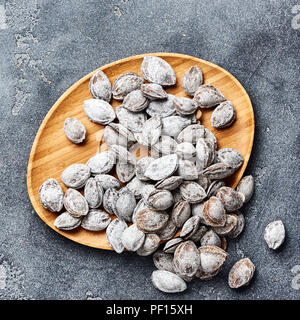 Salted apricot seeds on grey background. Apricot bones fried with salt in ashes. Stock Photo