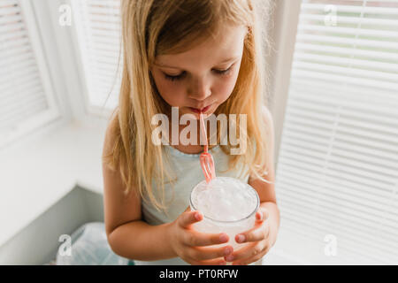 Blond little girl blowing milk bubbles Stock Photo