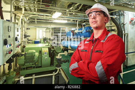 Ship's mechanic near marine diesel generators on a merchant ship in the engine room with all the piping, generators, turbins, etc. writing something d Stock Photo