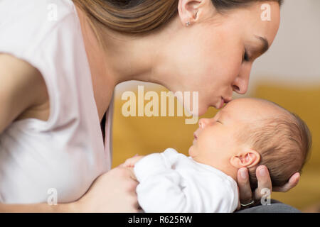 Loving Mother Cuddling Baby Son And Giving Him Kiss On Forehead Stock Photo