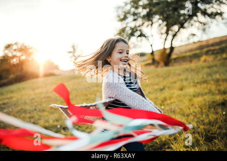 A small girl playing with a rainbow hand kite in autumn nature at sunset. Stock Photo