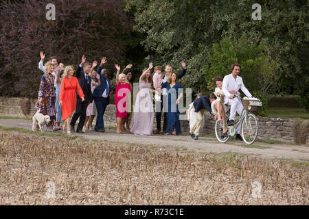 Wedding guests waving off newlyweds on bicycles Stock Photo