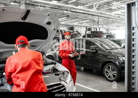 Two handsome auto mechanics in red uniform making wheel alignment with professional tools and computer at the car service Stock Photo