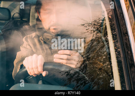 Front view of man driving car and texting on mobile phone which is dangerous and reckless behavior Stock Photo