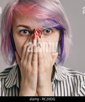 portrait of attractive, pretty, cute, charming, woman closed her mouth with hands and wide opened eyes, looking at camera, she can't believe her eyes, standing over grey background Stock Photo