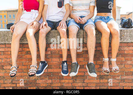 Legs of friends sitting together on a wall Stock Photo